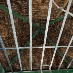 Montaż izolacji z wełny mineralnej w poddaszu, widoczne metalowe profile pod płyty karton-gips, drewniana konstrukcja dachu pomalowana na zielono i częściowo widoczna drabina.