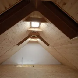 Poddasze z drewnianą boazerią, oknem dachowym i podłogą z płyt OSB, widoczne gniazdka elektryczne i otwór w podłodze.
