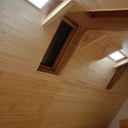 Łukasz Piotrowski Usługi Ogólnobudowlane - Drewniane wykończenie poddasza z oknami dachowymi, widoczne panele boazeryjne i konstrukcja wsporcza okien.