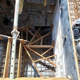 Zbrojenie fundamentu w szalunku, widoczne drewniane podpory i stalowe pręty, przygotowane do zalania betonem, z perspektywy z góry.