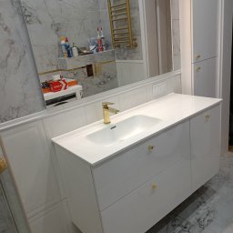 Łukasz Piotrowski Usługi Ogólnobudowlane - Nowoczesna łazienka z białą szafką pod umywalkę z złotymi uchwytami, marmurowe płytki na ścianach i podłodze, złoty grzejnik drabinkowy oraz duże lustro.