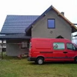 Dom jednorodzinny z nowym, grafitowym pokryciem dachowym z blachodachówki, widoczny czerwony samochód dostawczy na tle trawnika i rusztowania przy ścianie.