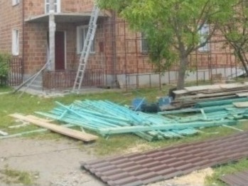 Budynek w trakcie remontu dachu, widoczne rusztowanie, drabina, stos niebieskich łat i brązowe dachówki na trawniku.