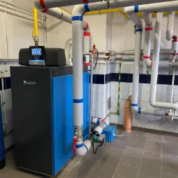 Nowoczesny, niebiesko-czarny piec gazowy Buderus z dotykowym panelem sterowania w kotłowni z rurami oznaczonymi kolorowymi taśmami.