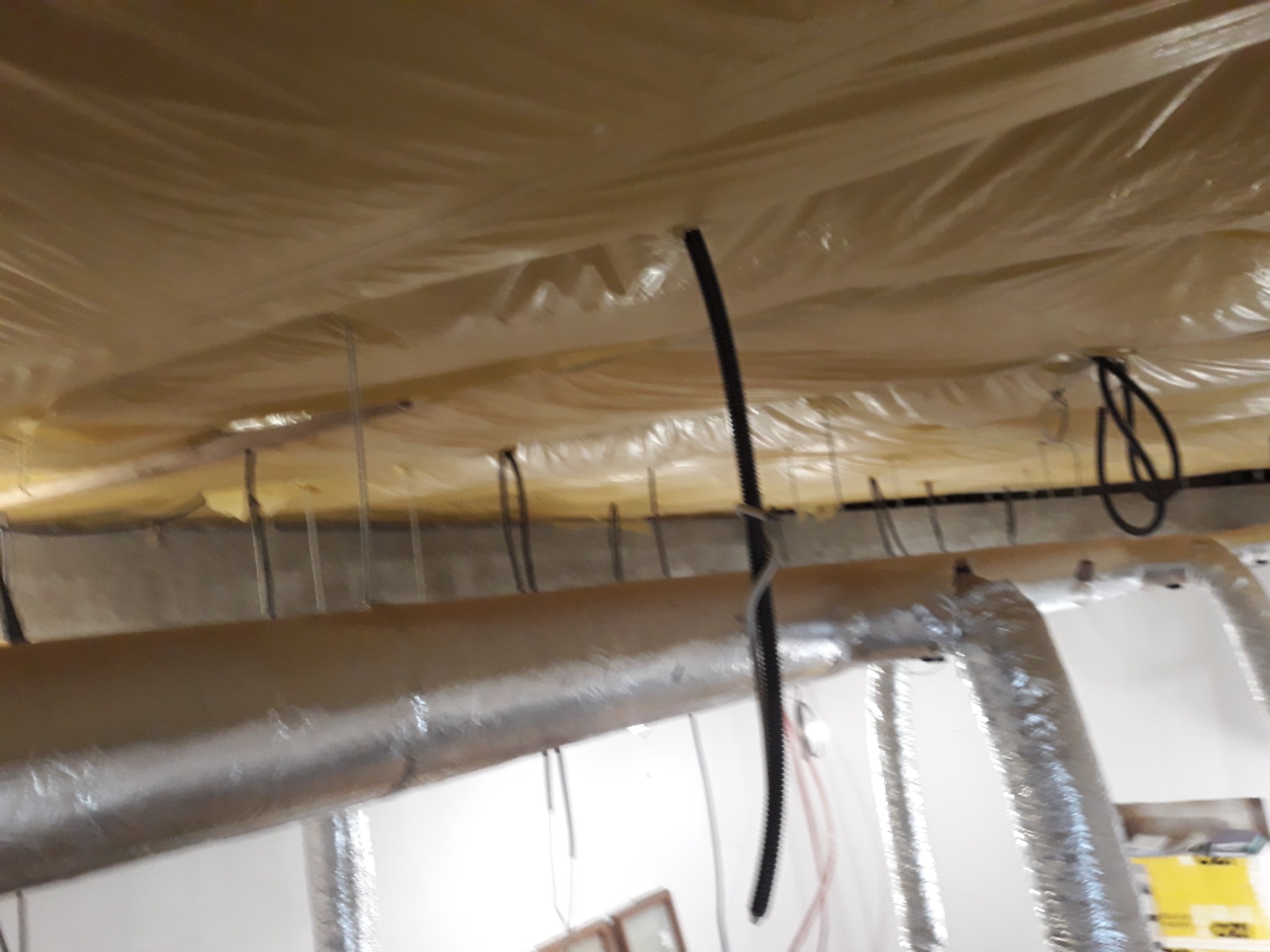 Folia ochronna na suficie podczas remontu, widoczne rury wentylacyjne i kable elektryczne