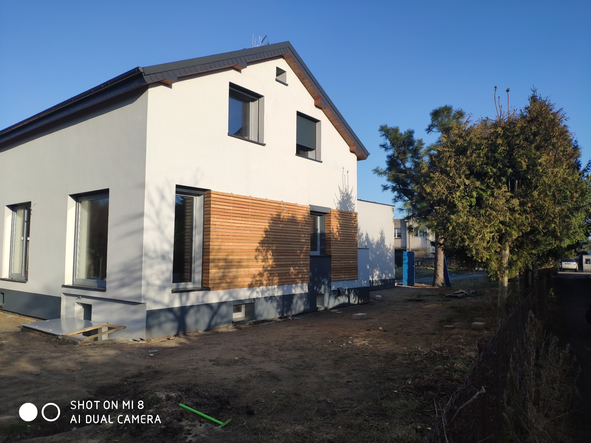 Nowoczesny dom jednorodzinny w Świdnicy z jasną elewacją, drewnianą okładziną i szarym dachem, widok z zewnątrz w słoneczny dzień.