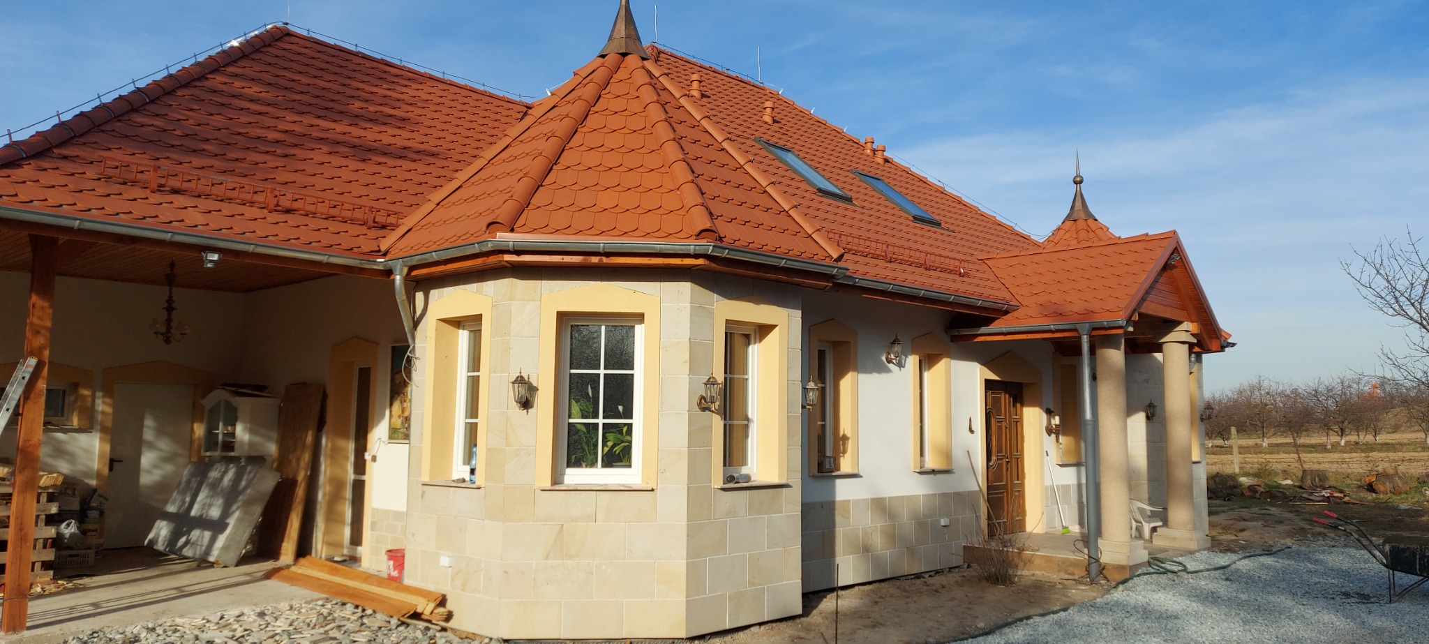 Dom jednorodzinny z czerwoną dachówką karpiówką, elewacją z piaskowca i ozdobnymi detalami architektonicznymi, widok z zewnątrz, ogród w tle.