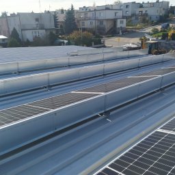 Energysat - Montaż paneli słonecznych na metalowym dachu budynku, widoczny żółty traktor w tle.