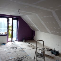 Piotr remonty - Poddasze w trakcie prac wykończeniowych: ściany i skosy pokryte płytami gips-karton, widoczne łączenia szpachlowane. Na podłodze rozłożona folia ochronna, drabina i narzędzia.