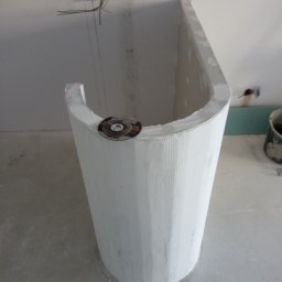 Piotr remonty - Nietypowa obudowa wanny z płyty karton gips, okrągły kształt, widoczne przewody elektryczne w ścianie, tarcza do cięcia na obudowie.