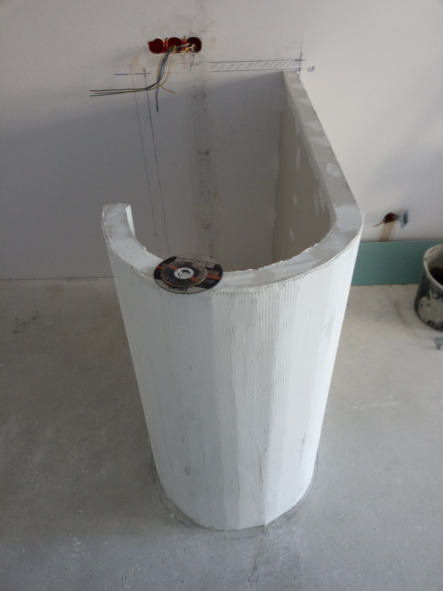 Nietypowa obudowa wanny z płyty karton gips, okrągły kształt, widoczne przewody elektryczne w ścianie, tarcza do cięcia na obudowie.