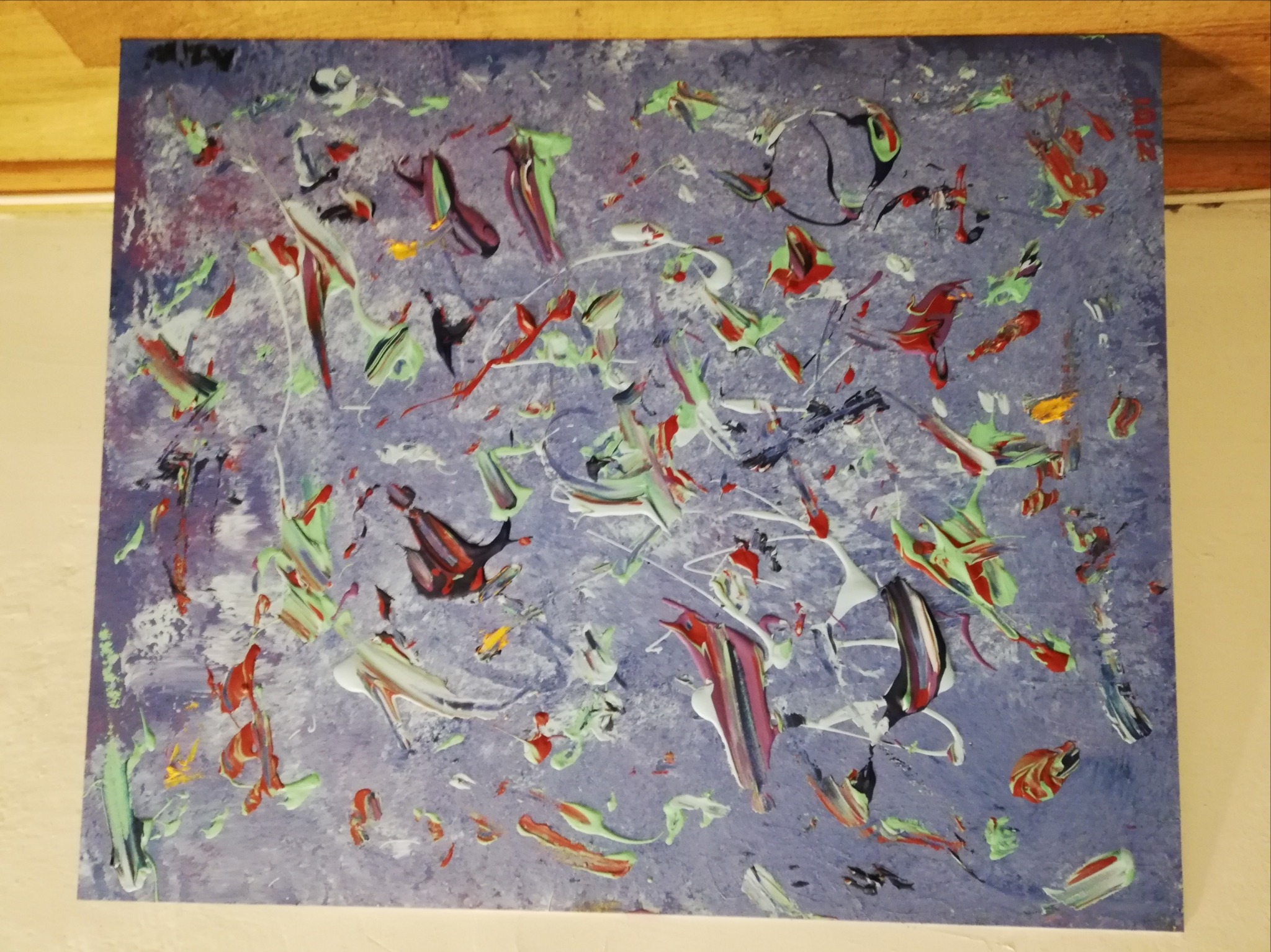 Abstrakcyjne malowidło na płótnie w odcieniach fioletu, zieleni, czerwieni i bieli, z wyraźnymi pociągnięciami pędzla i fakturą farby, umieszczone na tle ściany i drewnianej listwy.