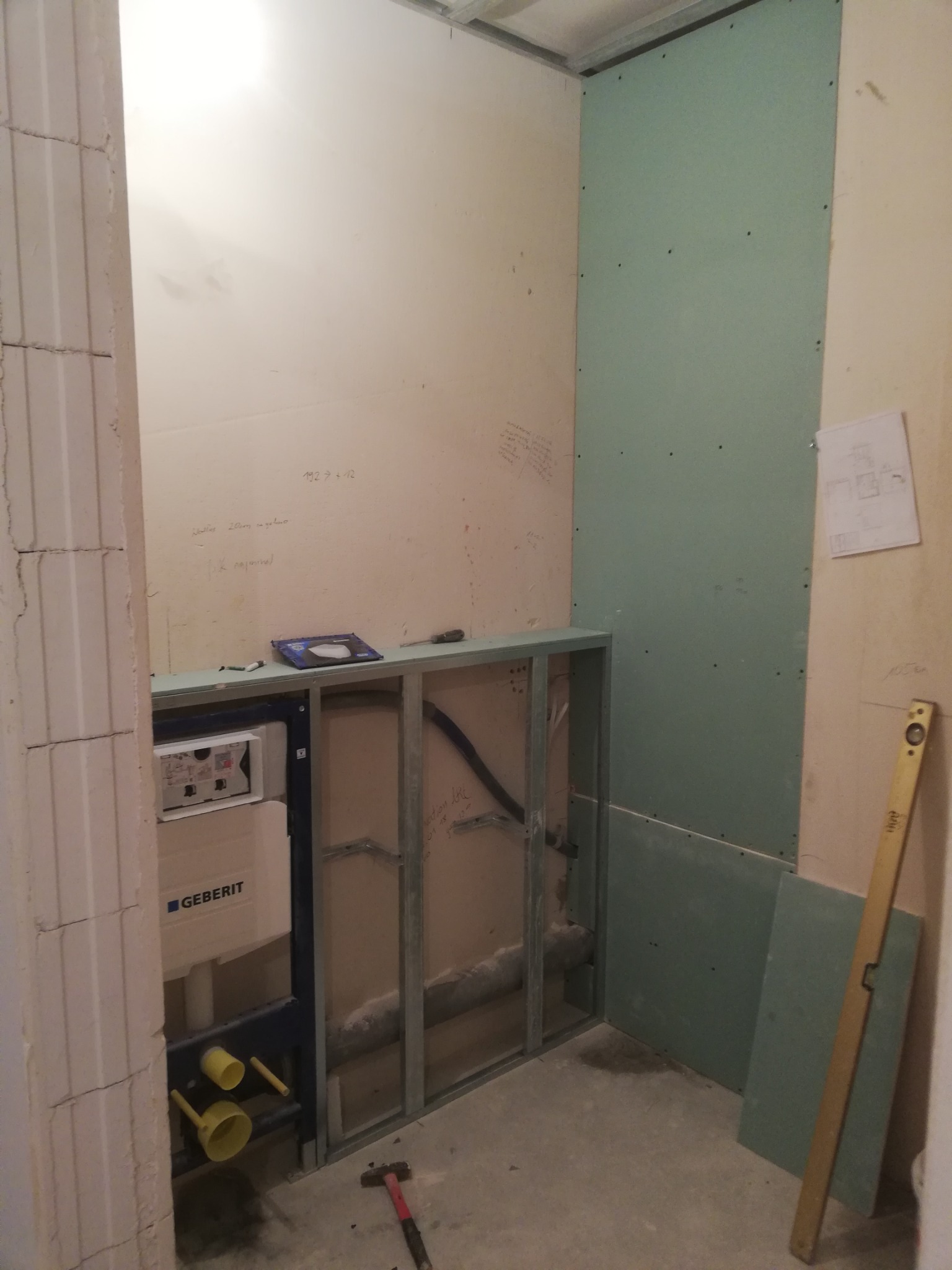 Łazienka w trakcie remontu w Warszawie: widoczny stelaż podtynkowy Geberit, częściowo zamontowana płyta karton-gips, poziomica oparta o ścianę, instalacja hydrauliczna w ścianie, ślady ołówka...