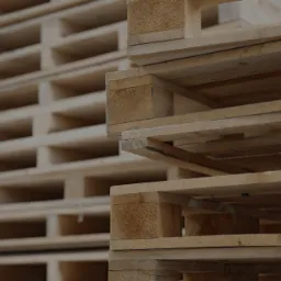 Stos jasnych, drewnianych palet ułożonych jeden na drugim, widoczne słoje drewna i struktura desek.