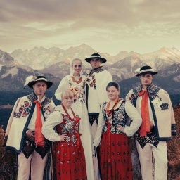 TLEN FOTO STUDIO - Krzysztof Tlen - Grupowe portretowe ujęcie pary młodej i gości weselnych w tradycyjnych strojach ludowych na tle górskiego krajobrazu z widocznymi szczytami Tatr.