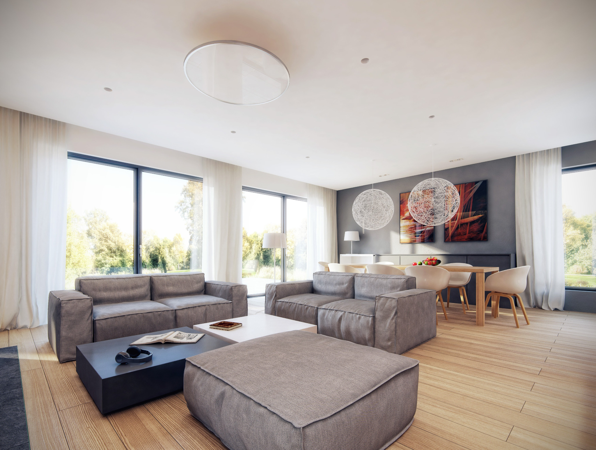 Jasne, przestronne wnętrze z dwoma szarymi sofami, czarnym stolikiem kawowym z książką i słuchawkami, pufem oraz jadalnią z drewnianym stołem i białymi krzesłami, oświetlone naturalnym światłem...