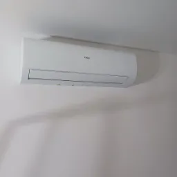 Biały klimatyzator Haier zamontowany na jasnej ścianie, widok z dołu, minimalistyczny design, oświetlenie dzienne.