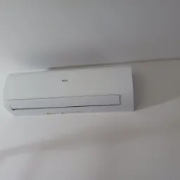 Biały klimatyzator Haier zamontowany na jasnej ścianie, z widocznymi detalami obudowy i subtelnym cieniem, sugerujący świeżą instalację w nowoczesnym wnętrzu.