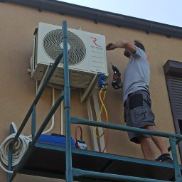 STELAR Przedsiębiorstwo Handlowo - Usługowe Greta Turska - Montaż klimatyzatora Rotenso na elewacji budynku. Instalator na rusztowaniu, używa wkrętarki. Widoczne przewody i narzędzia.