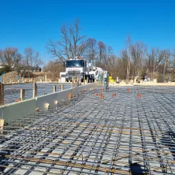 Zbrojenie fundamentu z widocznym betonowozem w tle, ujęcie w słoneczny dzień.