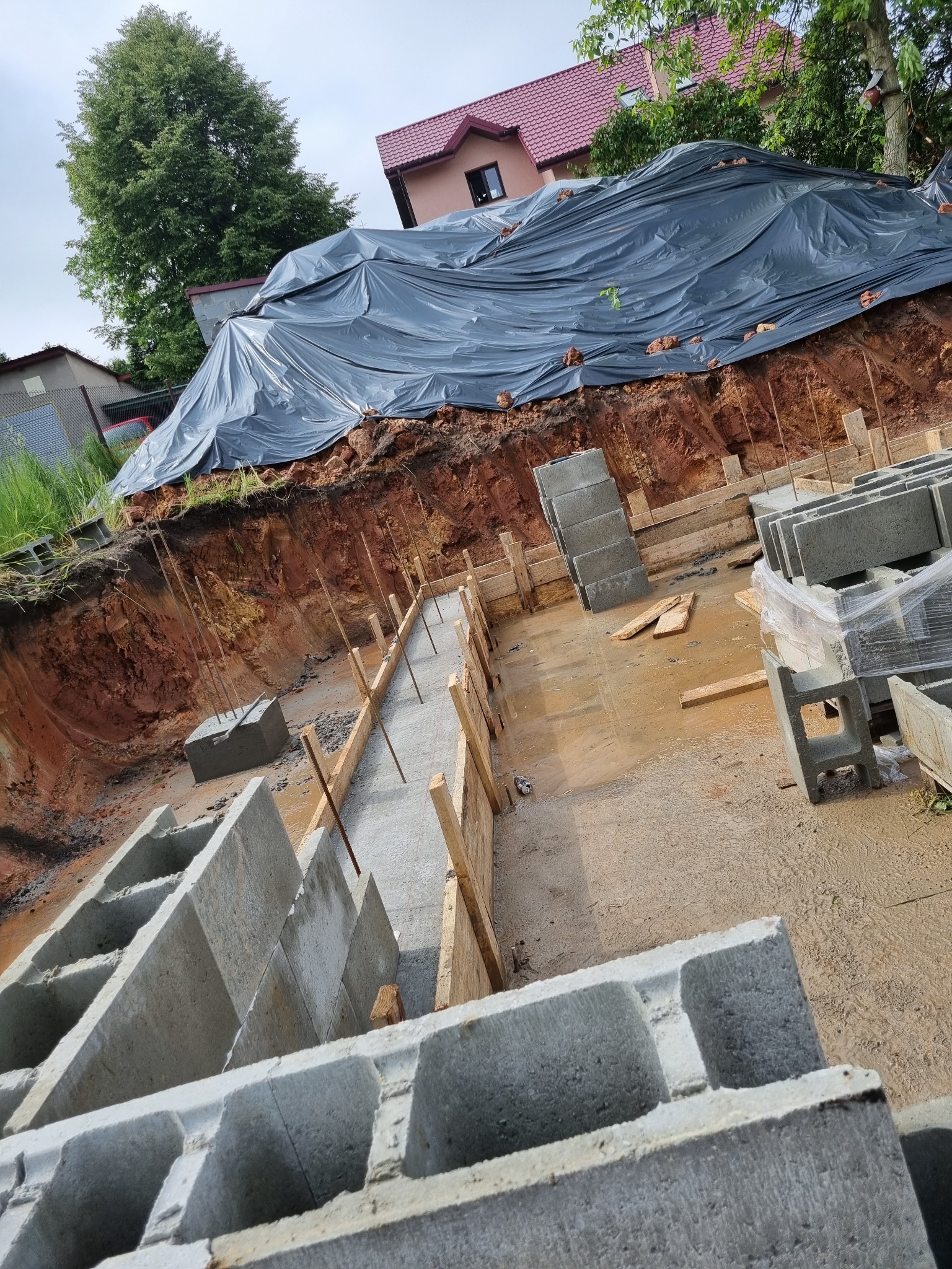 Budowa fundamentów: wykop zabezpieczony folią, betonowa wylewka w szalunku, bloczki betonowe na mokrym podłożu.
