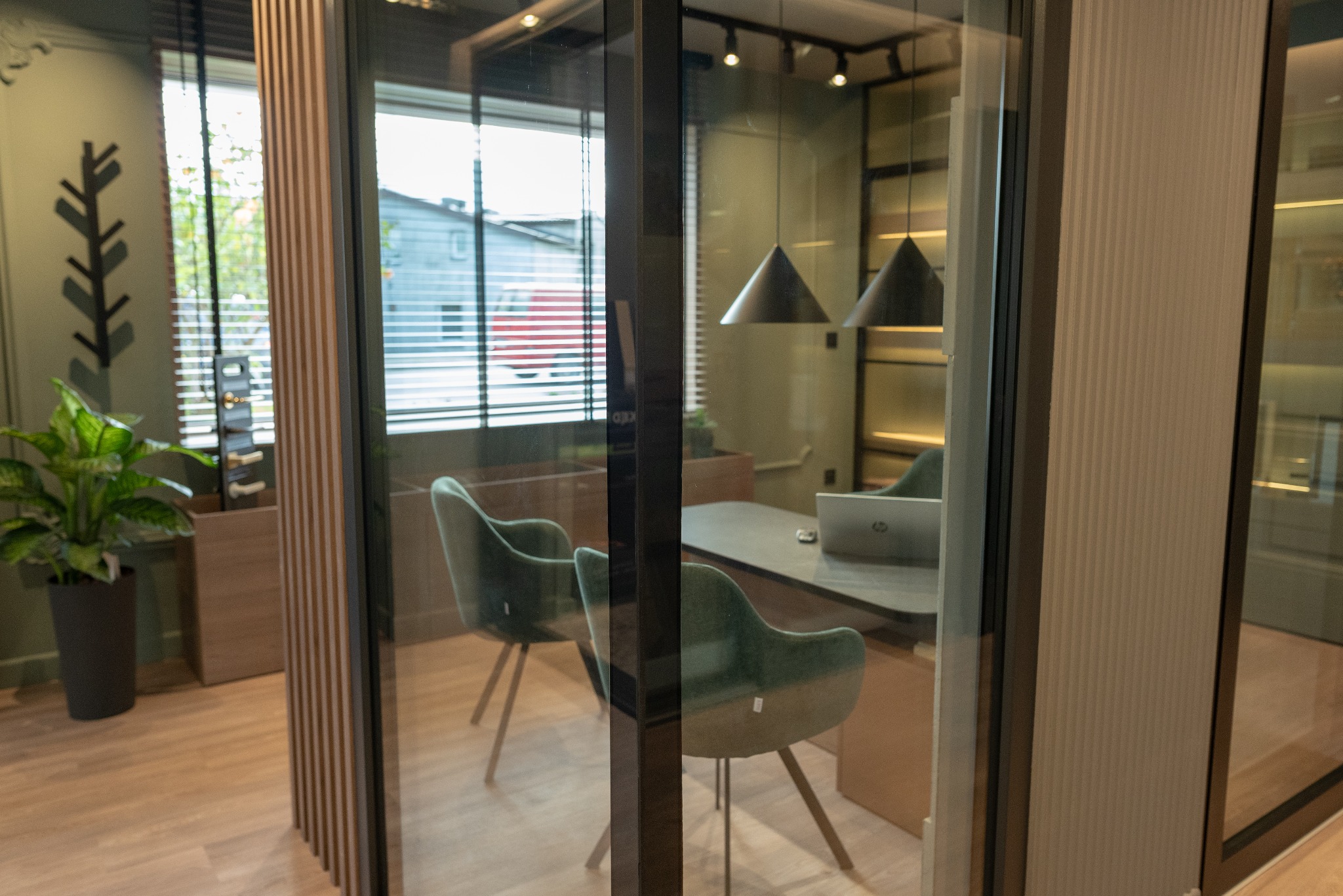 Okno PCV z szybami zespolonymi tworzące przeszkloną ścianę biurową, widoczne biurko, krzesła i lampy wewnątrz, z zewnątrz widok na budynek mieszkalny.