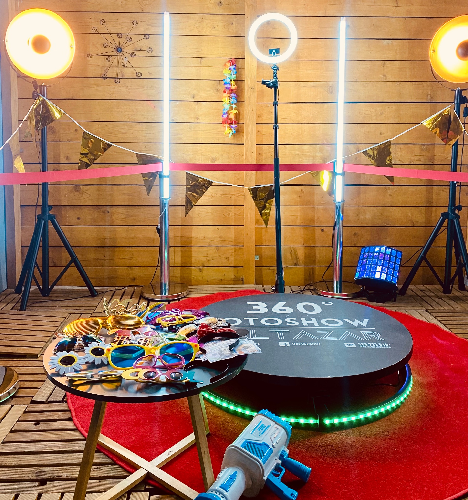 Instalacja fotobudki 360 stopni z rekwizytami, oświetleniem LED i dekoracjami na tle drewnianej ściany.