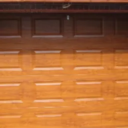 Zamknięta segmentowa brama garażowa w kolorze drewna, z ościeżnicą z czerwonej cegły, widoczna z bliska.