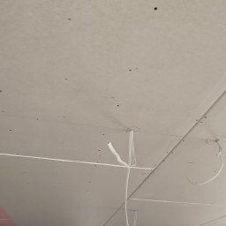 APM Marcin Woś Ambasador Rockwoll - Sufit z płyt gipsowo-kartonowych w trakcie montażu, widoczne przewody elektryczne. Ujęcie z dołu, okno w tle. Ślady po szpachlowaniu.