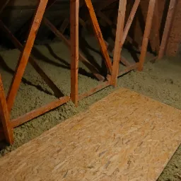 Fragment poddasza z drewnianą konstrukcją i izolacją z wełny mineralnej, częściowo pokrytej płytą OSB. Widoczne oznaczenia na elementach konstrukcyjnych.