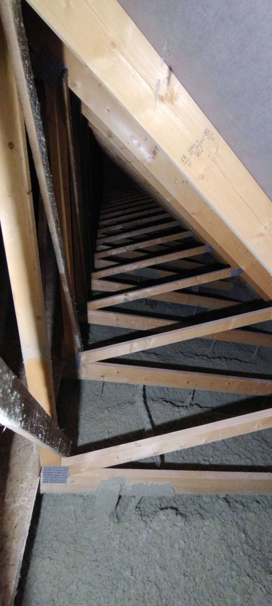 Skośny widok na ocieplone wełną mineralną poddasze z drewnianą konstrukcją więźby dachowej, widoczne elementy metalowe łączące drewniane belki.