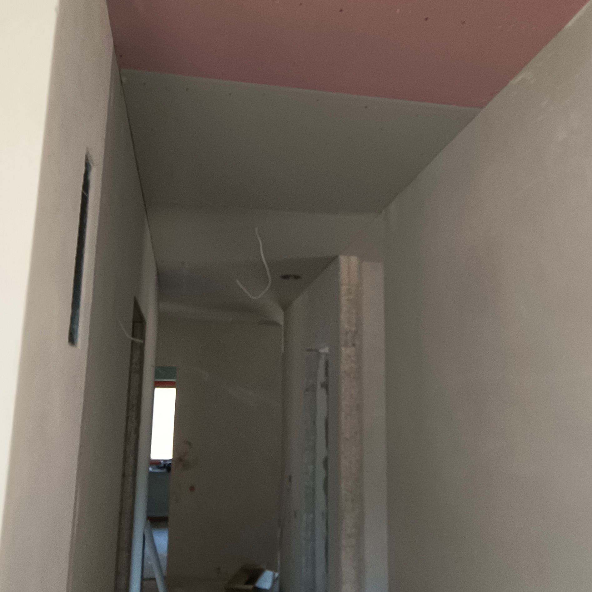 Korytarz w trakcie wykańczania: ściany po szpachlowaniu, sufit z płyt karton-gips, widoczne przewody. W tle okno i drabina.