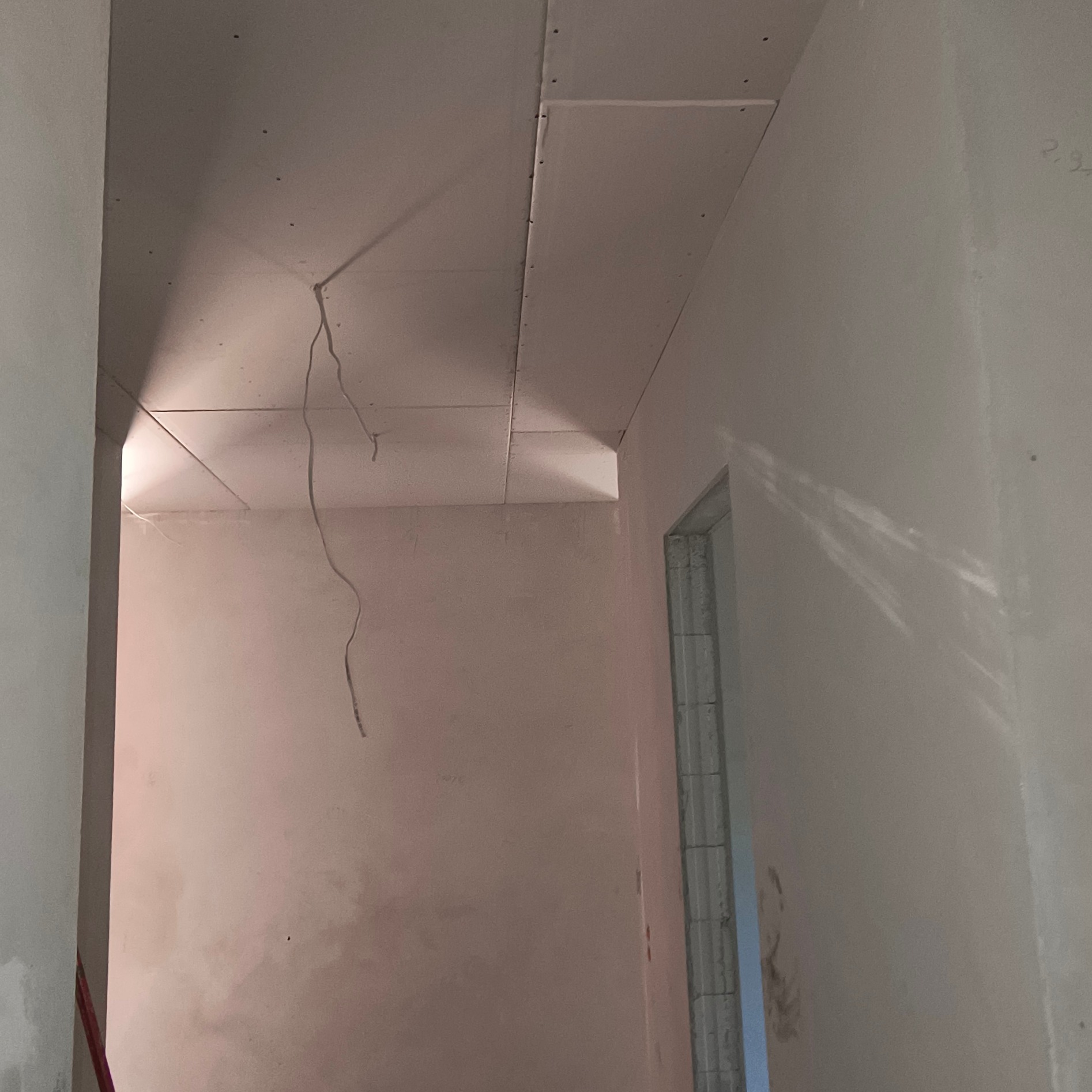 Montaż płyt karton-gips na suficie w pomieszczeniu z widoczną instalacją elektryczną i surowymi ścianami. Kątowe ujęcie z perspektywą wnętrza.