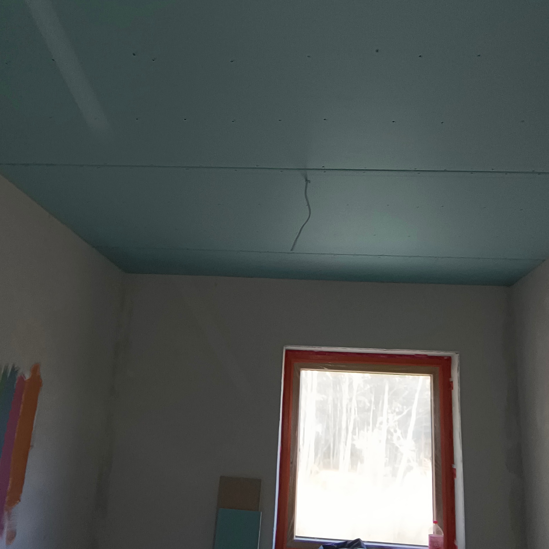 Zabudowa z płyty GK na suficie w pokoju z oknem. Widoczny kabel wystający z sufitu, przygotowany do podłączenia lampy. Ściany przygotowane do malowania.