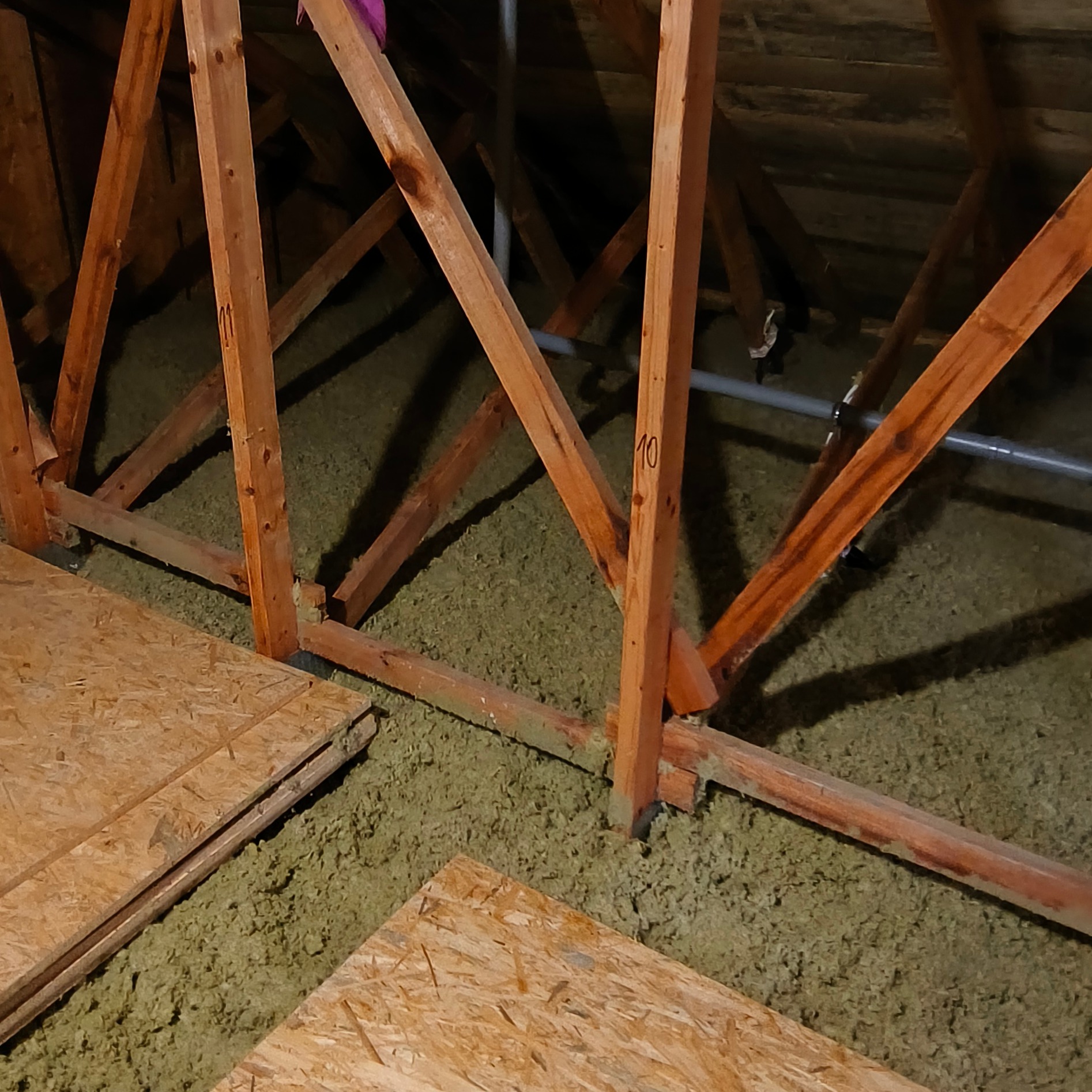 Poddasze z drewnianą konstrukcją i ociepleniem z wełny mineralnej, częściowo pokryte płytami OSB. Widoczne oznaczenia numeracji na elementach drewnianych.