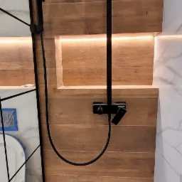 Nowoczesna kabina prysznicowa z czarną armaturą, drewnopodobnymi płytkami i podświetlaną wnęką, widoczny odpływ liniowy.