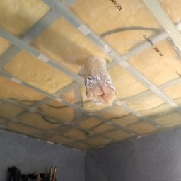 Wykończenia wnętrz - Poddasze z widoczną izolacją z wełny mineralnej marki Isover, zabezpieczoną folią, w trakcie montażu na ruszcie z profili metalowych, z otworem na rurę wentylacyjną obłożoną folią aluminiową.