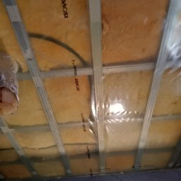 Wykończenia wnętrz - Poddasze w trakcie izolacji wełną mineralną Isover, zabezpieczone folią, widoczne metalowe profile konstrukcyjne.