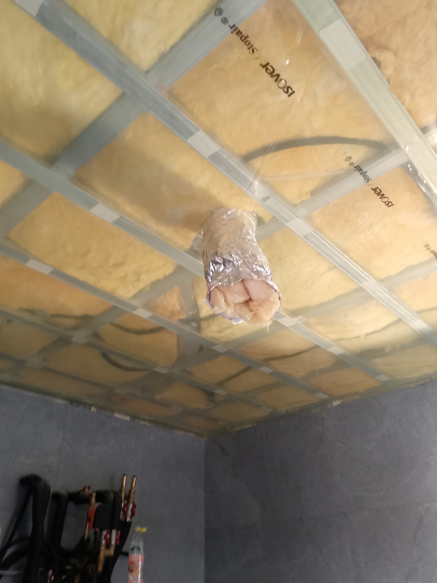 Poddasze z widoczną izolacją z wełny mineralnej marki Isover, zabezpieczoną folią, w trakcie montażu na ruszcie z profili metalowych, z otworem na rurę wentylacyjną obłożoną folią aluminiową.