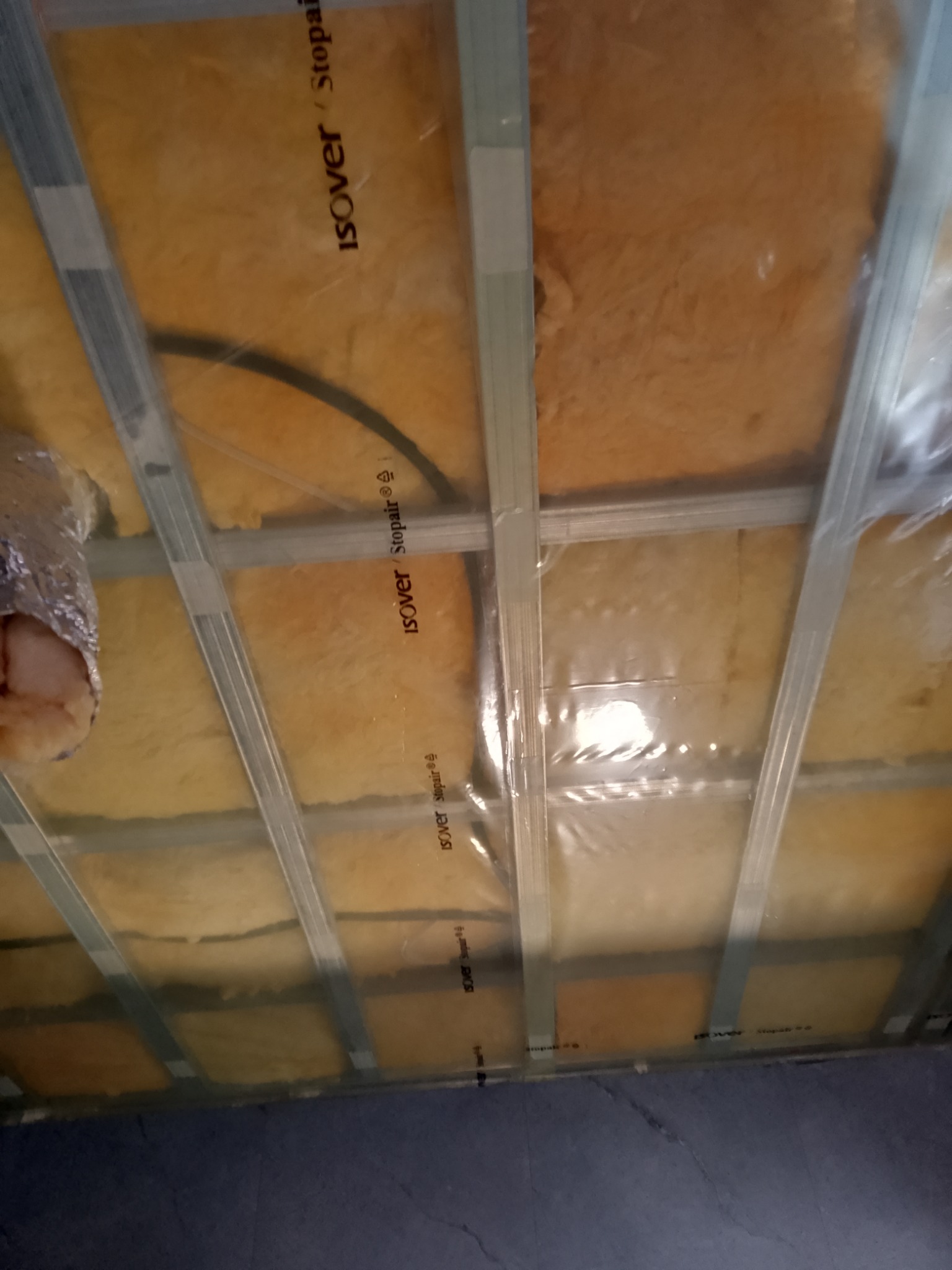 Poddasze w trakcie izolacji wełną mineralną Isover, zabezpieczone folią, widoczne metalowe profile konstrukcyjne.