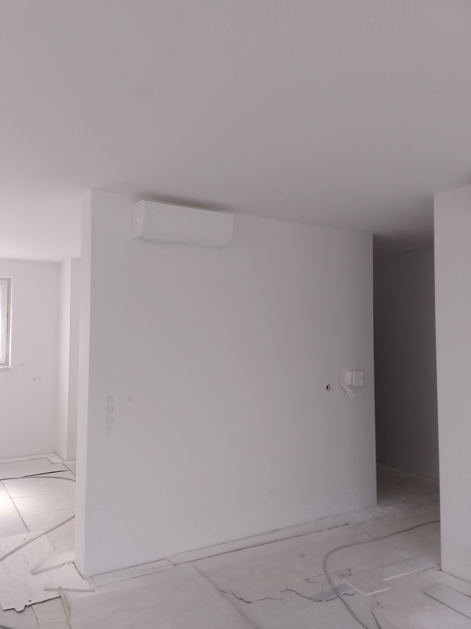 Białe wnętrze po remoncie. Widoczne gładkie ściany, zakryty klimatyzator, przygotowane podłoże pod panele. Minimalistyczny design, jasne oświetlenie, świeżo po pracach.