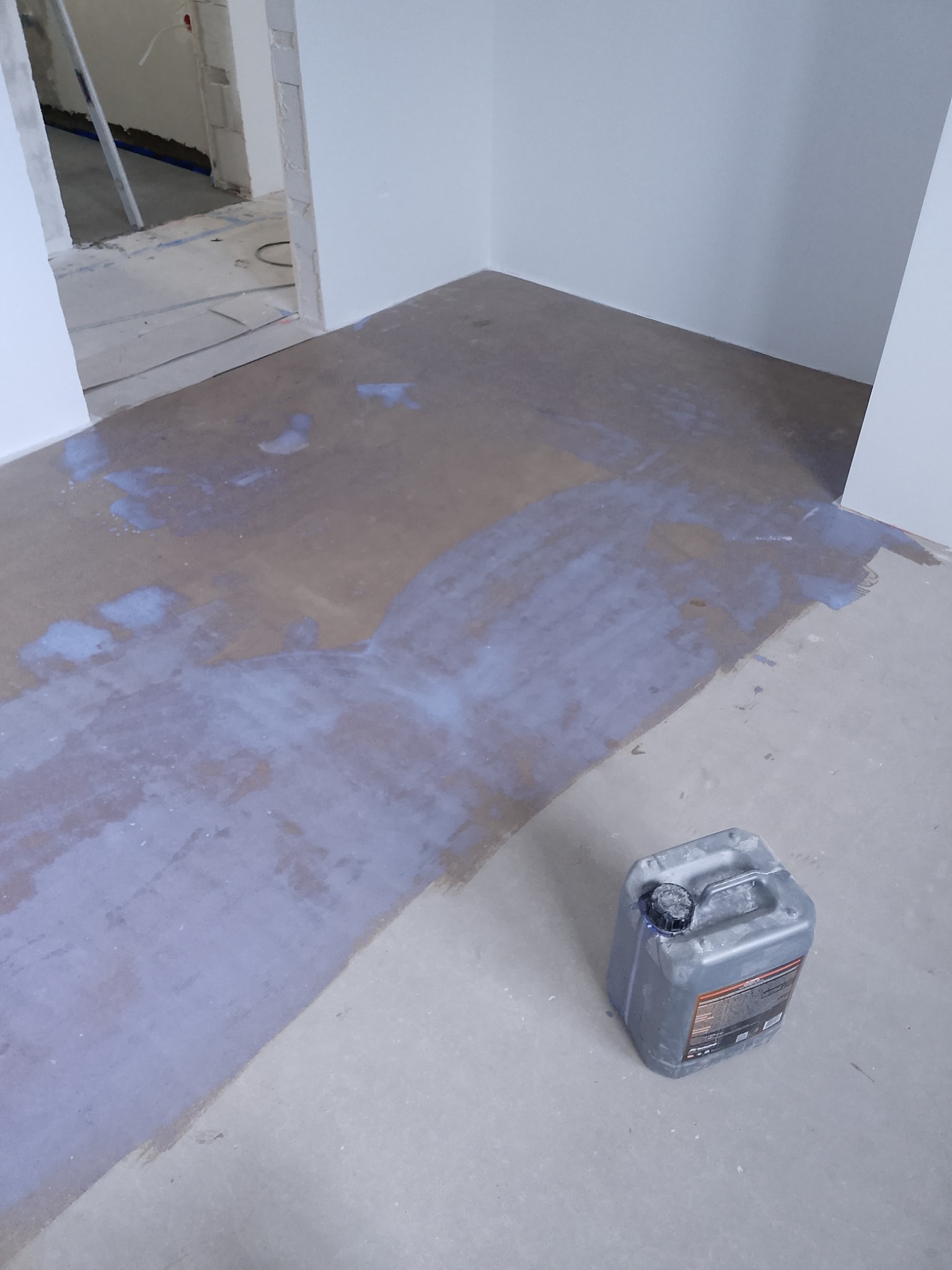 Gruntowanie podłogi w pomieszczeniu przed dalszymi pracami wykończeniowymi. Widoczny kanister z preparatem gruntującym.