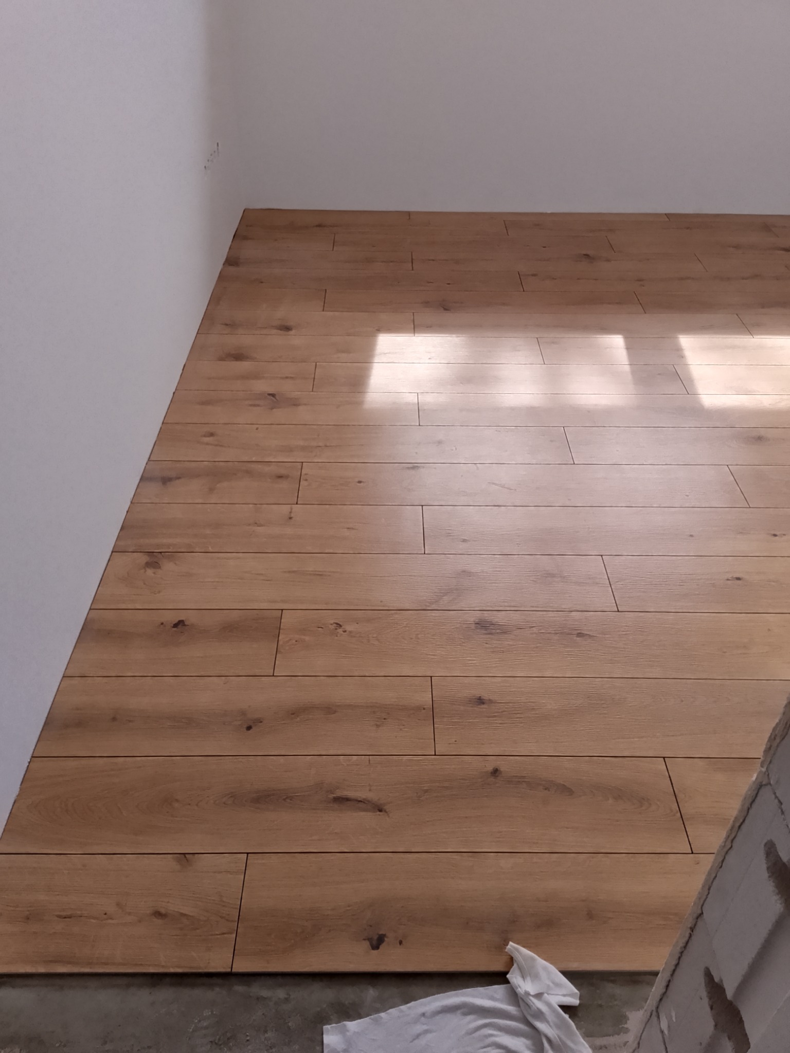 Ułożona podłoga z paneli imitujących drewno, z widocznym fragmentem ściany i podłoża w trakcie prac. Naturalne światło podkreśla strukturę paneli.