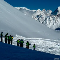 Grupa narciarzy w kaskach i jaskrawych kamizelkach na tle ośnieżonych gór, widok z dołu.