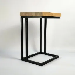 Stolik pomocniczy z blatem z jasnego drewna i czarną, metalową podstawą w kształcie litery C, na białym tle.