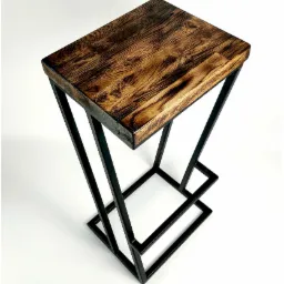 Stolik barowy z blatem z ciemnego, lakierowanego drewna o wyraźnym usłojeniu i geometryczną, spawana podstawą z czarnych, metalowych profili.
