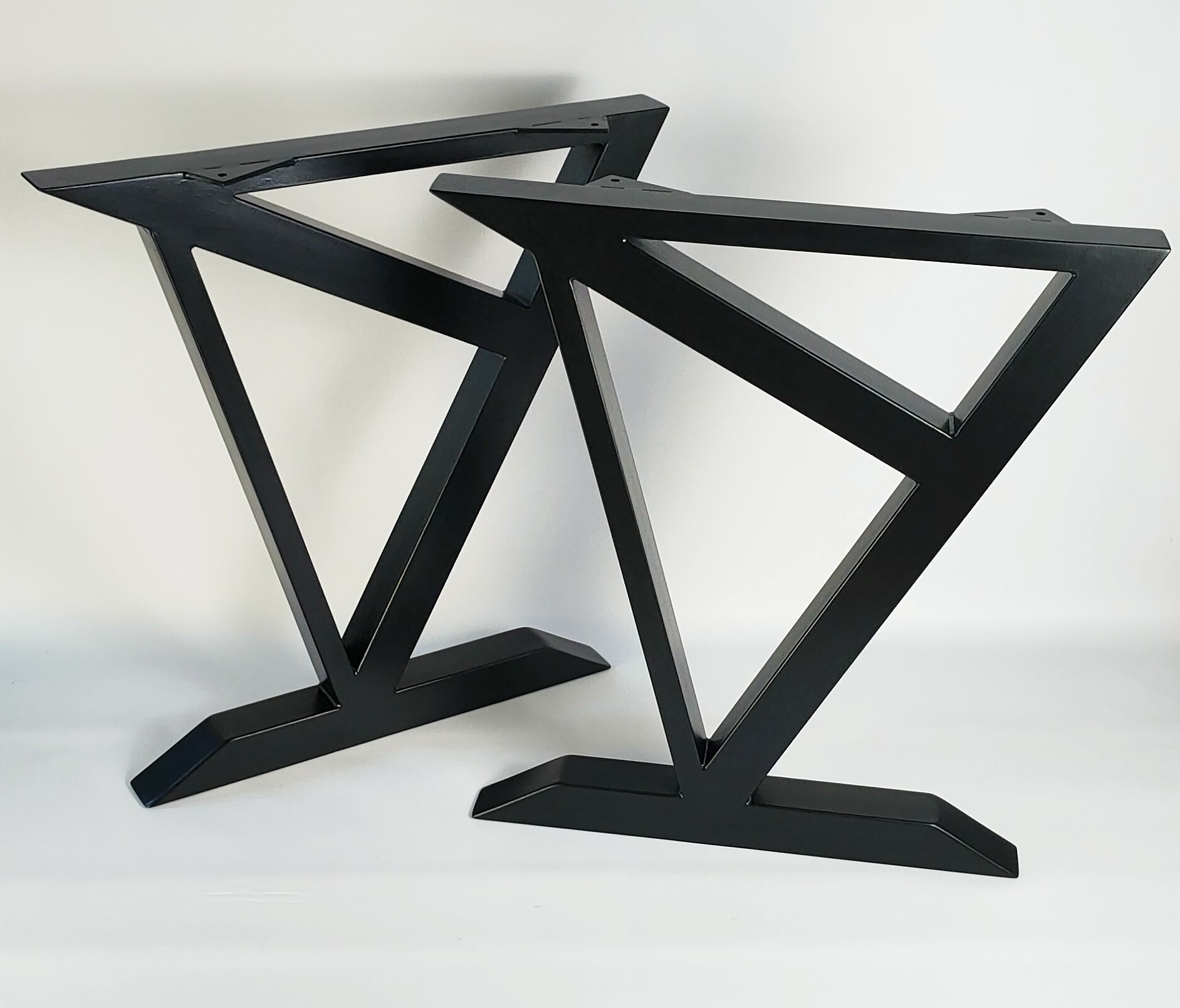 Dwie metalowe nogi do stołu w kolorze czarnym, o geometrycznym kształcie, ustawione na białym tle, gotowe do montażu blatu.