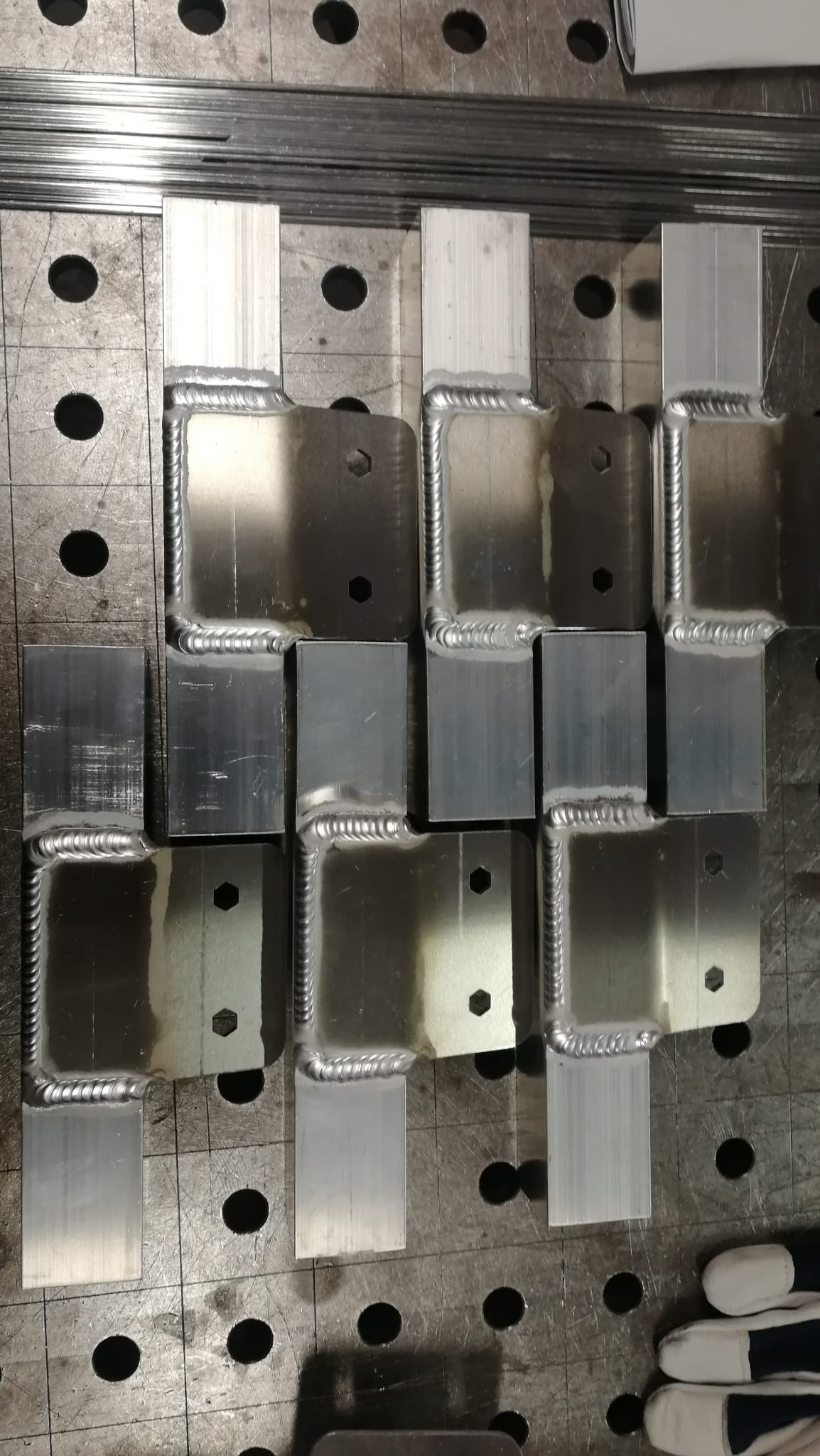 Metalowe elementy z widocznymi spawami na stole spawalniczym w Toruniu, ukazujące precyzyjne łączenia i otwory montażowe.