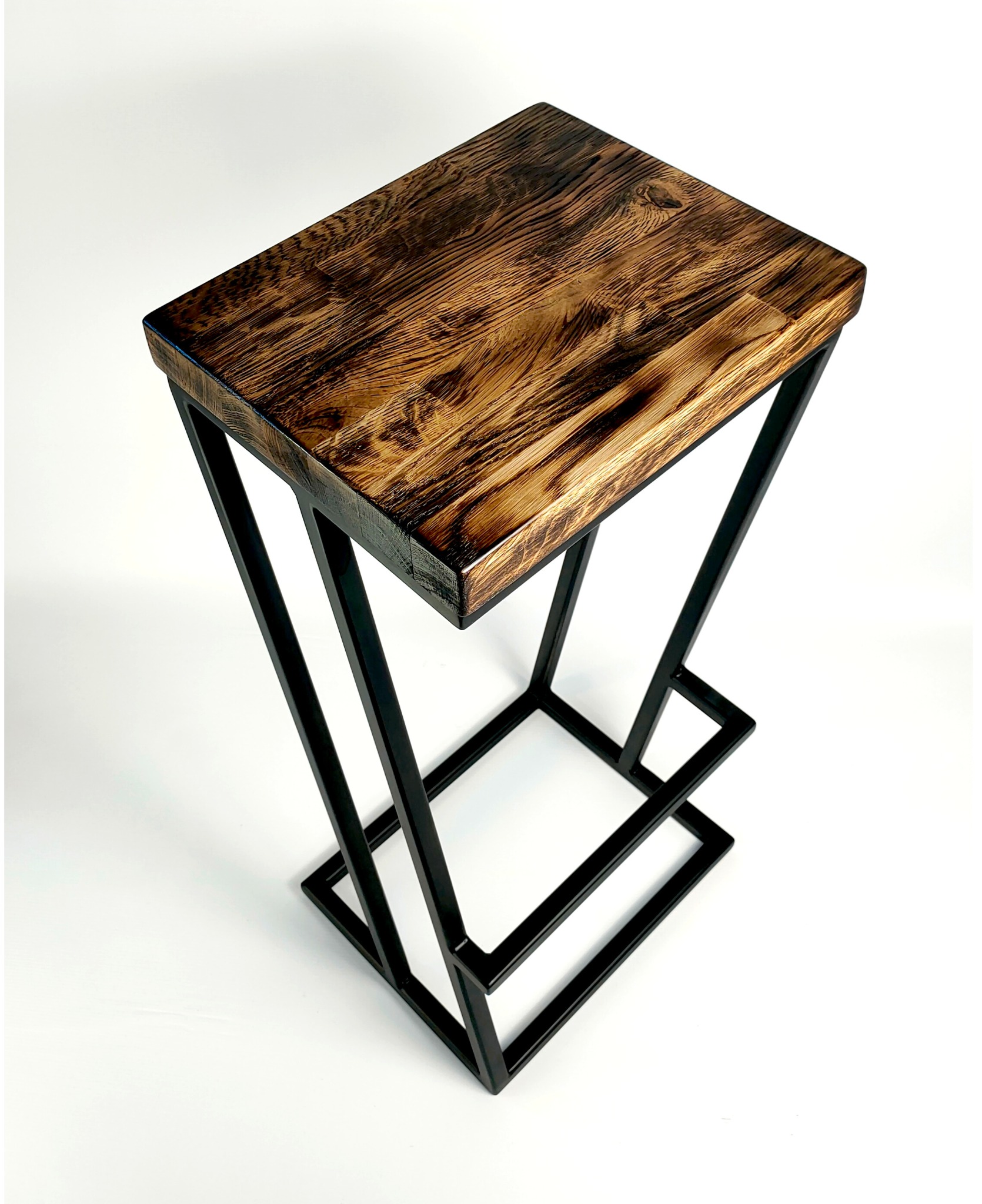 Stolik barowy z blatem z ciemnego, lakierowanego drewna o wyraźnym usłojeniu i geometryczną, spawana podstawą z czarnych, metalowych profili.