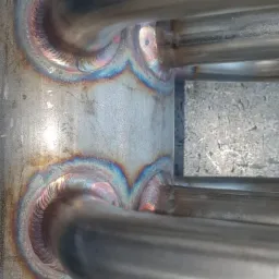 Szczegółowe ujęcie spawanych rur ze stali nierdzewnej, widoczne tęczowe przebarwienia na spoinach, świadczące o wysokiej temperaturze podczas spawania.